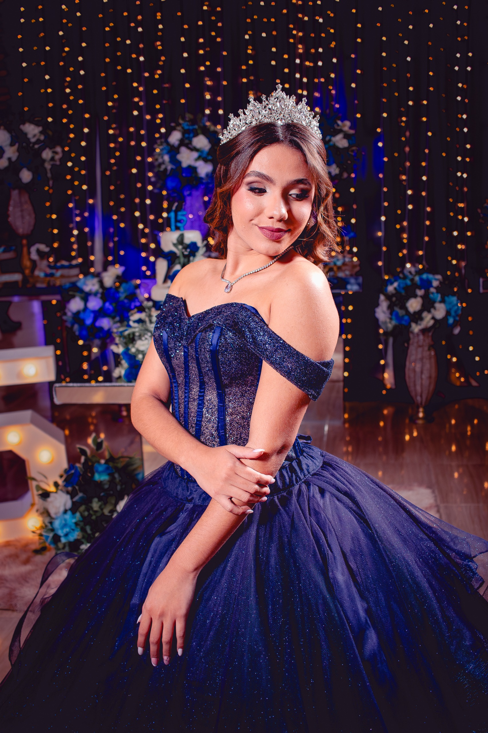 Debutante com tiara e vestido azul brilhante, em frente a cortina de luzes