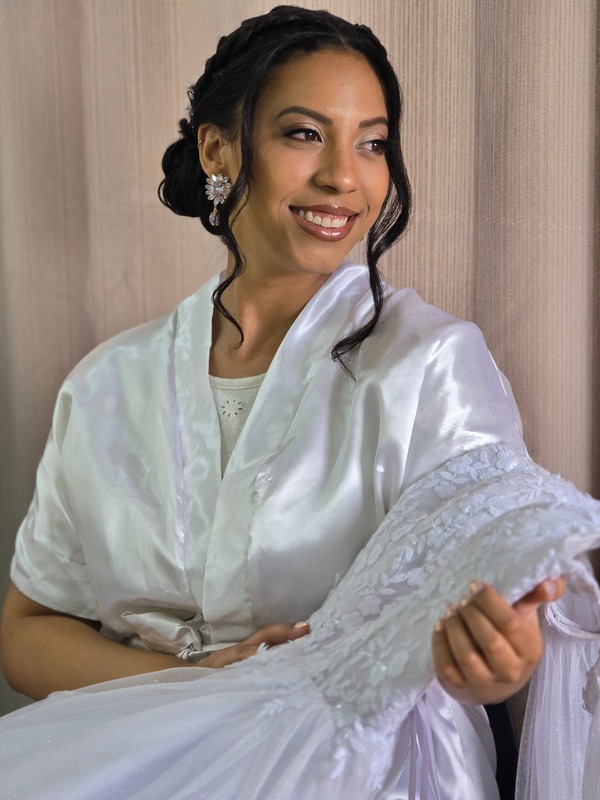 Noiva de robe de cetim com penteado preso e mechas soltas, segurando o vestido de renda