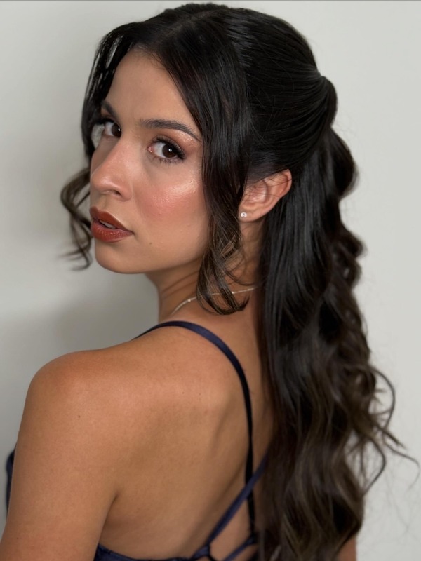 Mulher olhando por cima do ombro com penteado semipreso ondulado e maquiagem iluminada
